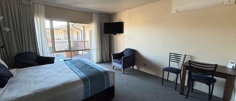 Habitación de hotel con cama, dos sillas, escritorio, televisor y balcón con cortinas.