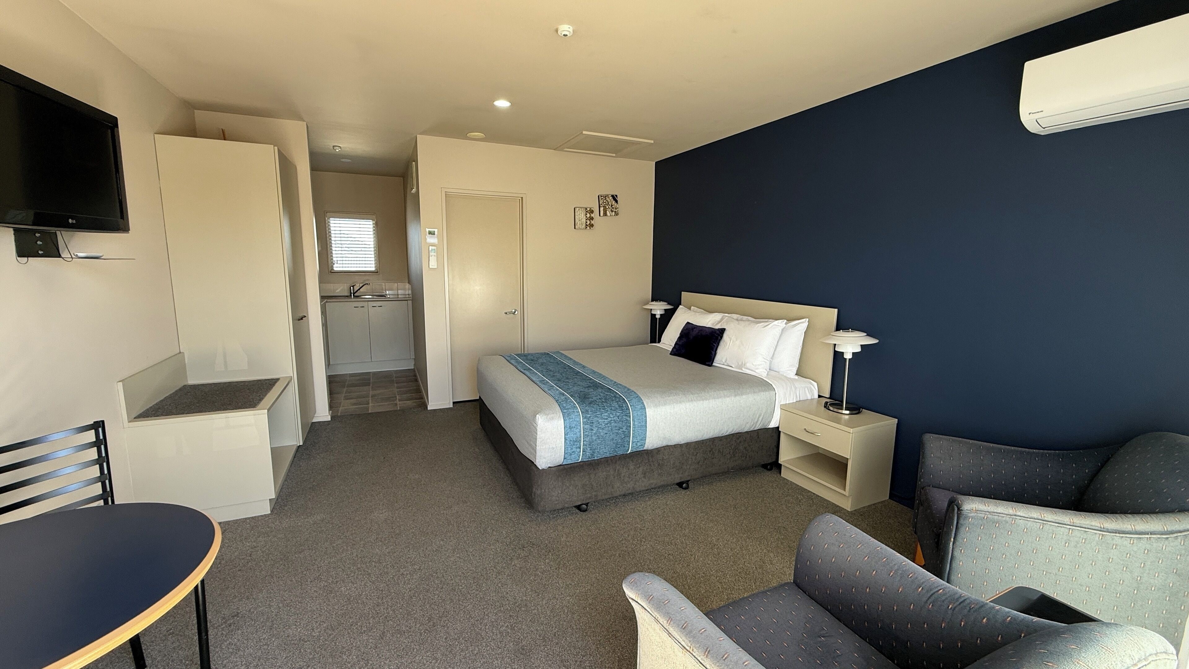 Een hotelkamer met een bed, nachtkastje, lamp, stoel, bureau en een televisie.