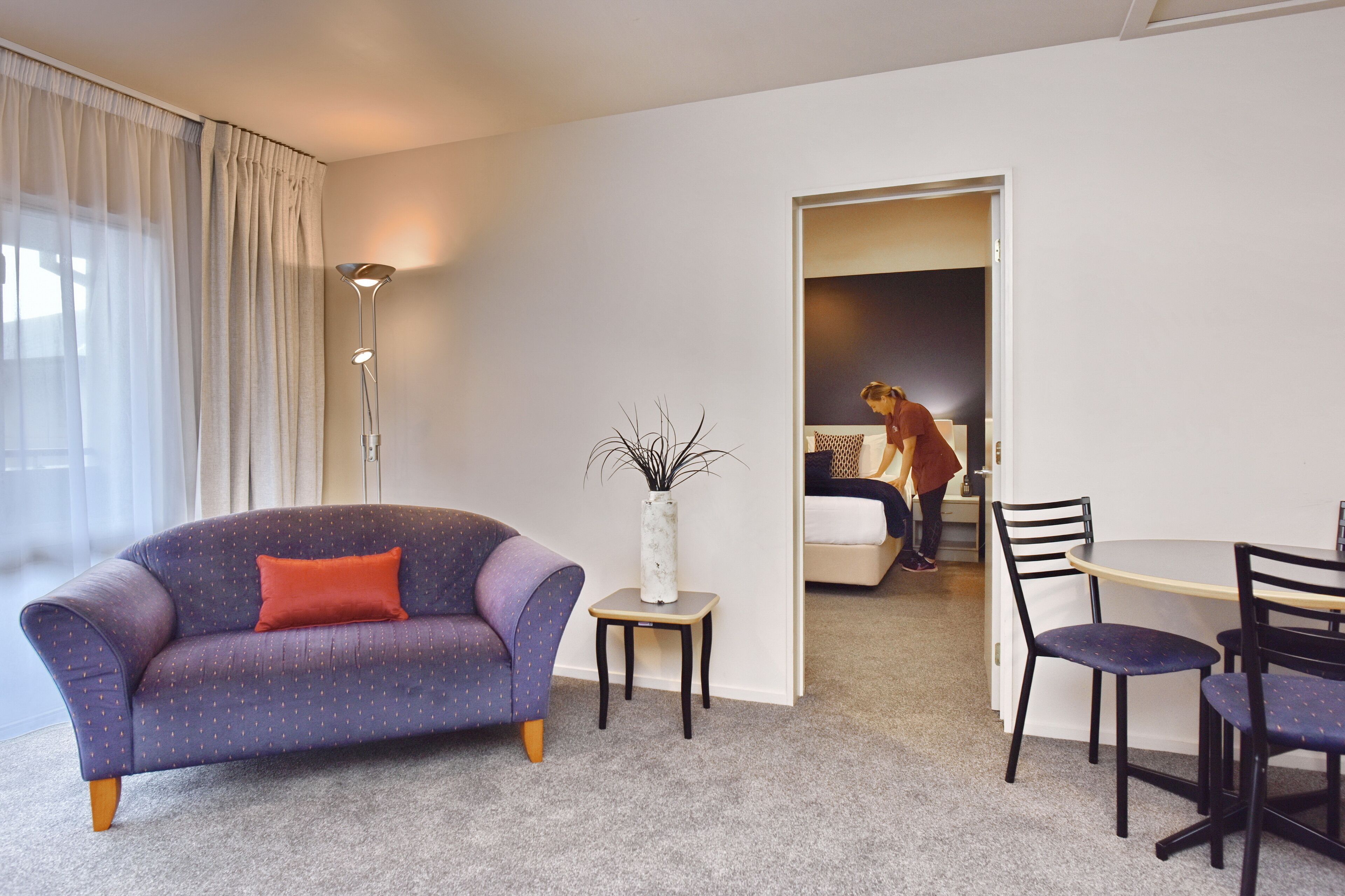 A modern living room with a purple sofa, a small white vase, and a dining area with a table and chairs.