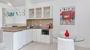 A modern kitchen with white cabinetry, a built-in oven, and a glass table with a red vase. - Linger A While Chalet (Tamborine Mountain)