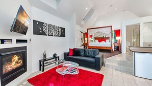 A modern hotel room with a fireplace, a bed with a canopy, a dining area, and a bathroom. - Linger A While Chalet (Tamborine Mountain)