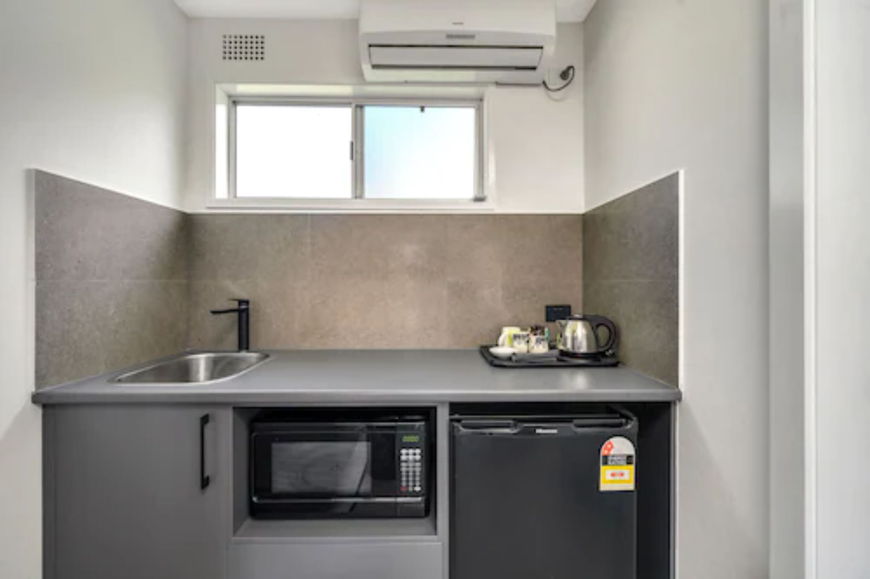A compact kitchen with a built-in microwave, a dishwasher, and a sink. There is a window above the sink, and a coffee maker on the counter.