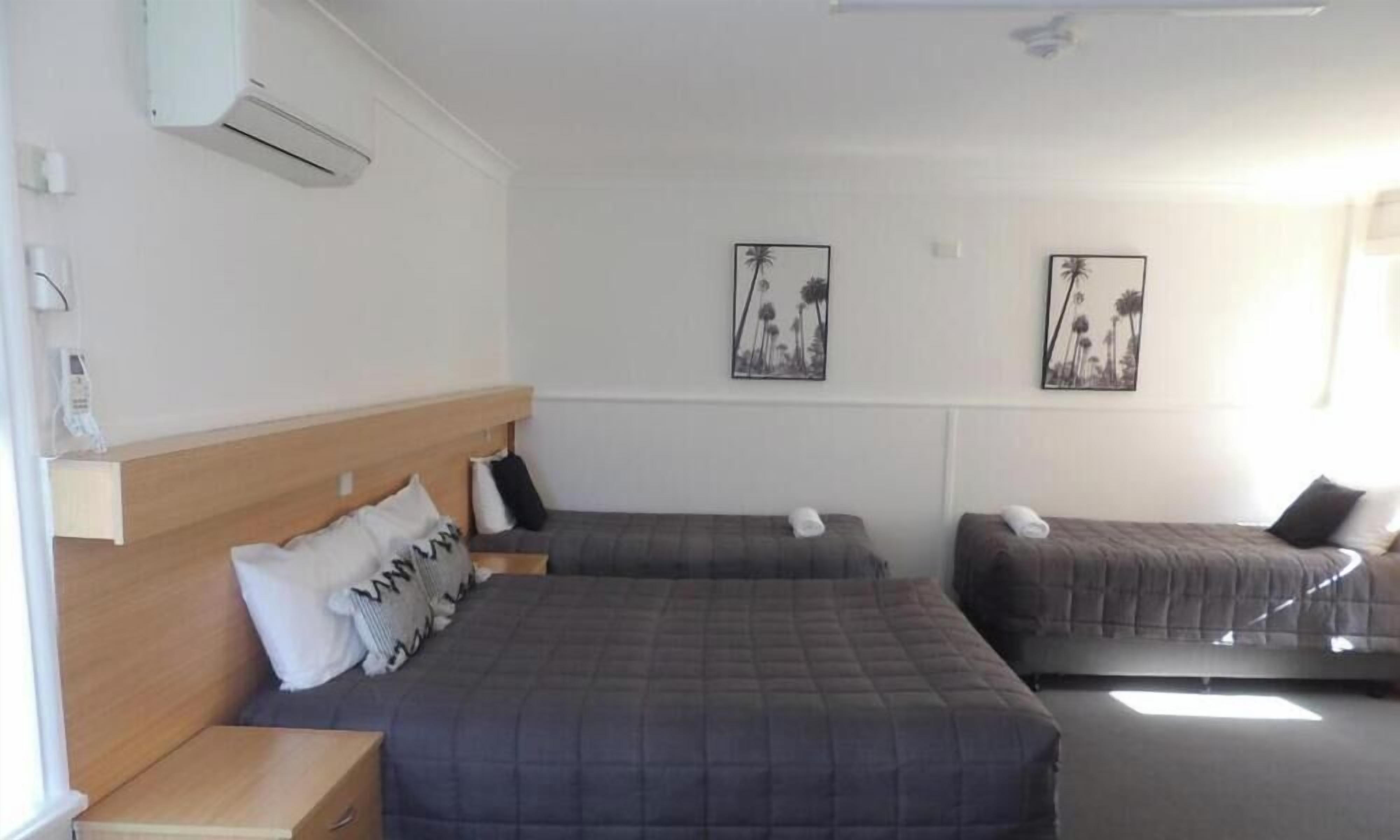 A hotel room with two beds, a wooden headboard, and two wall-mounted air conditioning units.
