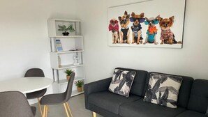 A modern living room with a dark grey sofa, two grey chairs, a white round table, and a wall-mounted shelf with a plant. - Kiama Motel 617 (Kiama)