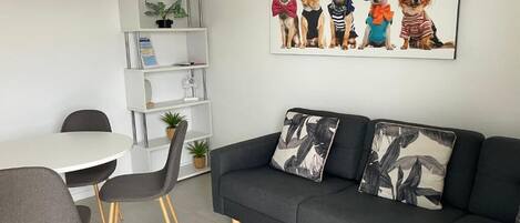 A modern living room with a dark grey sofa, two grey chairs, a white round table, and a wall-mounted shelf with a plant.