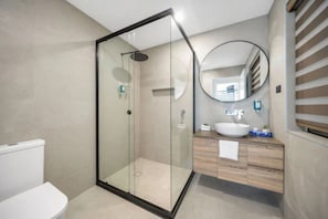 A modern bathroom with a glass-enclosed shower, a white toilet, a wooden vanity with a sink, and a round mirror.