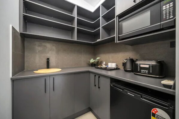 A modern kitchen with grey cabinets, a microwave, a coffee machine, and a sink.
