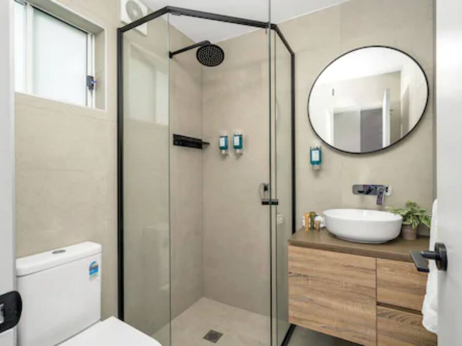 A modern bathroom with a glass-enclosed shower, a round mirror, and a wooden vanity.
