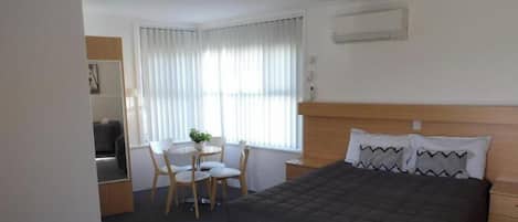 Habitación de hotel con cama, escritorio con silla, una mesita con planta y ventana con cortinas.