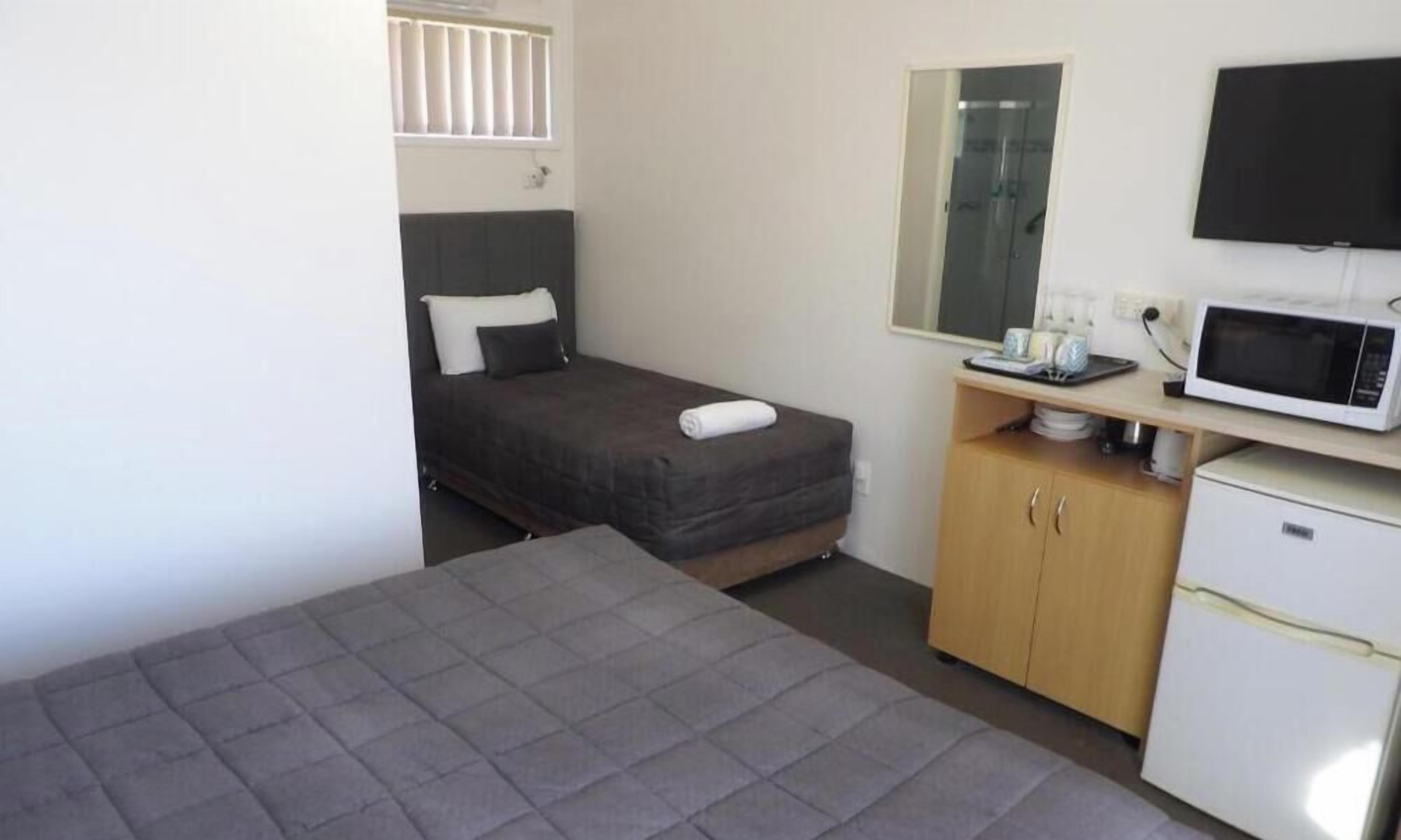 Una habitación pequeña y funcional con cama, escritorio, microondas y refrigerador.