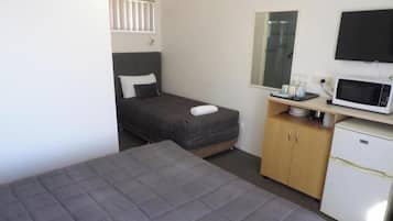 Una habitación pequeña y funcional con cama, escritorio, microondas y refrigerador.