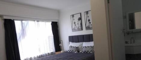 Een slaapkamer met een bed, een raam met gordijnen en een spiegel aan de muur.