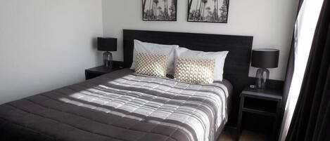 A neatly made bed with a striped bedspread, two pillows, and two bedside tables with lamps.