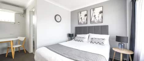 A modern hotel room with a large bed, bedside tables, a desk, and a chair.