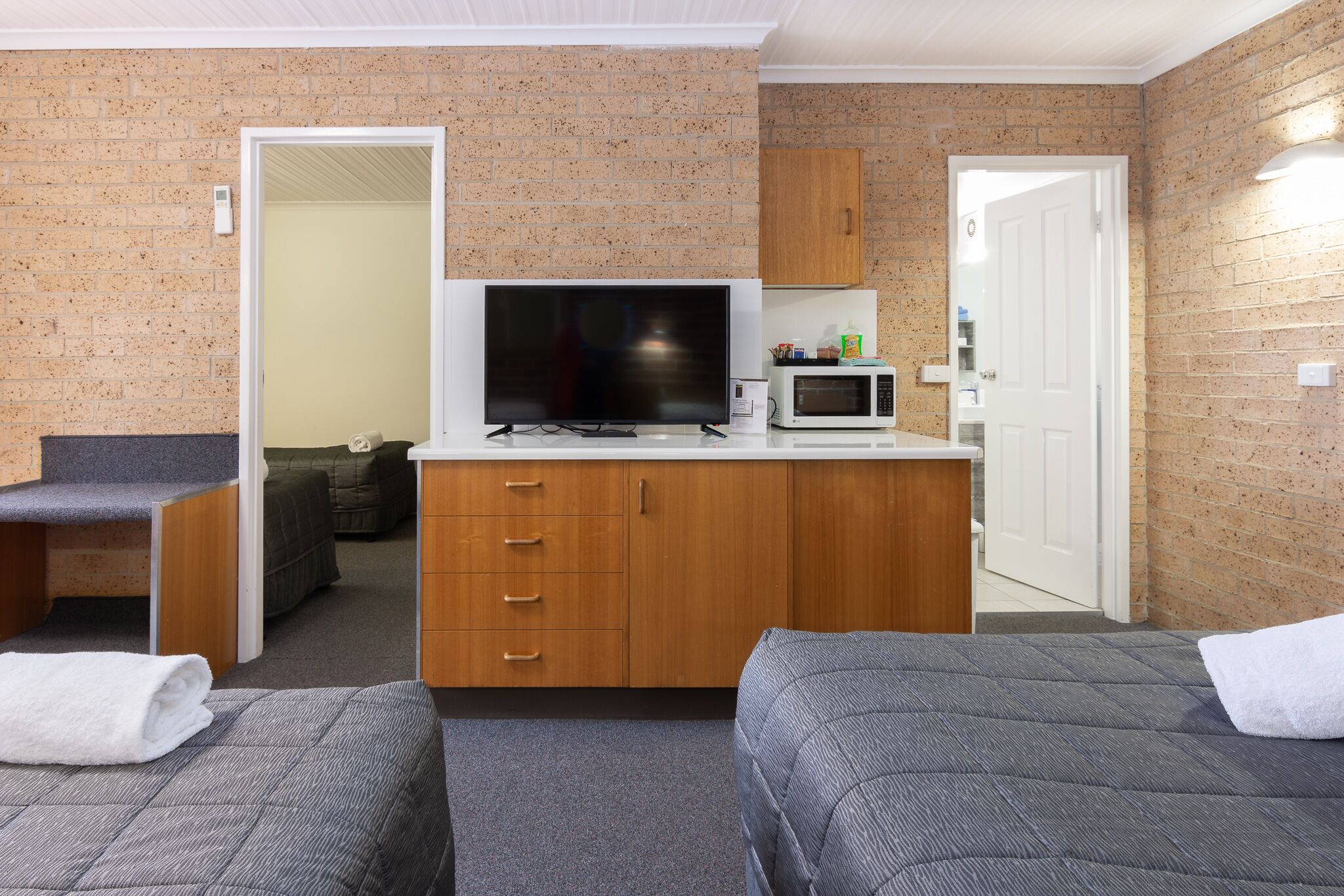 A compact hotel room with a kitchenette, a television, and two single beds.