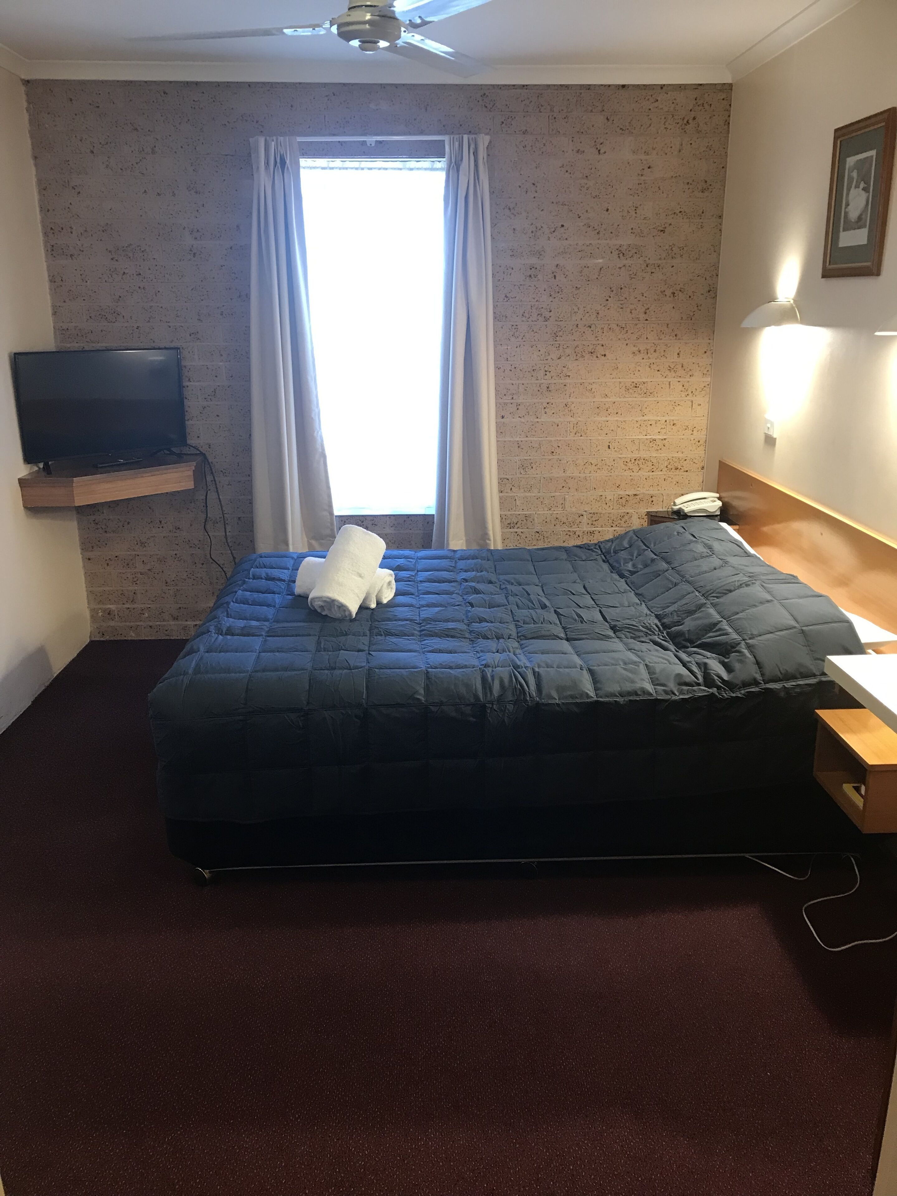 A hotel room with a bed, a television on a shelf, a telephone, and a window with curtains.