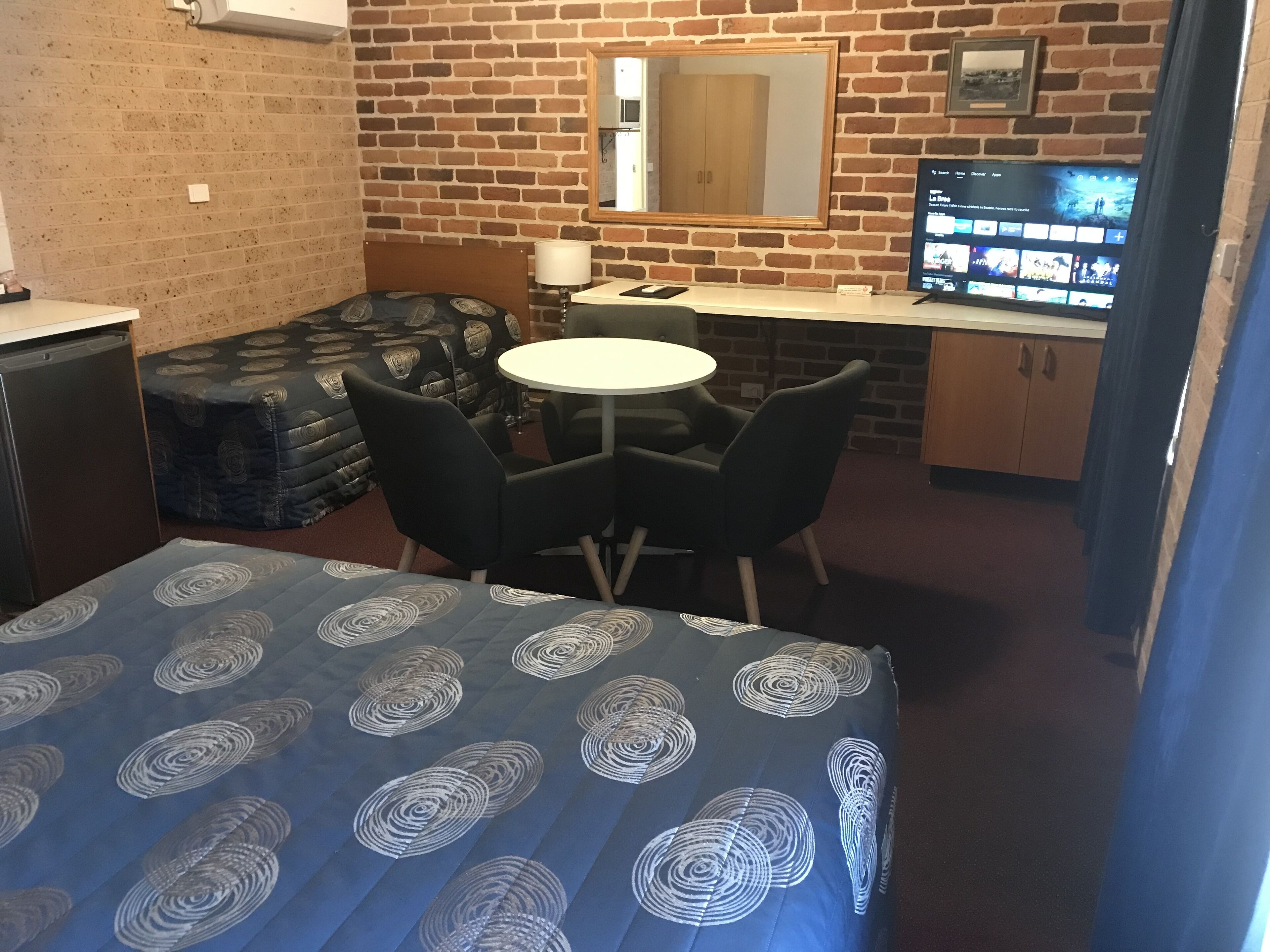Une pièce de taille modeste comprenant un lit, une petite table avec des chaises, un téléviseur et un coin cuisine.