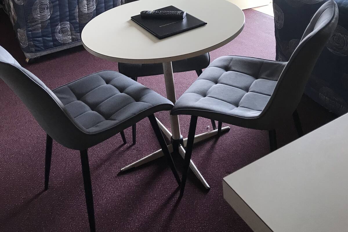 A room with a bed, a table with two chairs, a door, and a painting on the wall.