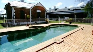 A swimming pool with a brick deck, a brick building with a chimney, and a fenced area. - Lochinvar House B&B (Lochinvar)
