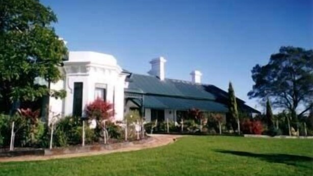 A white building with a green roof, surrounded by a well-maintained lawn and trees. - Lochinvar House B&B (Lochinvar)