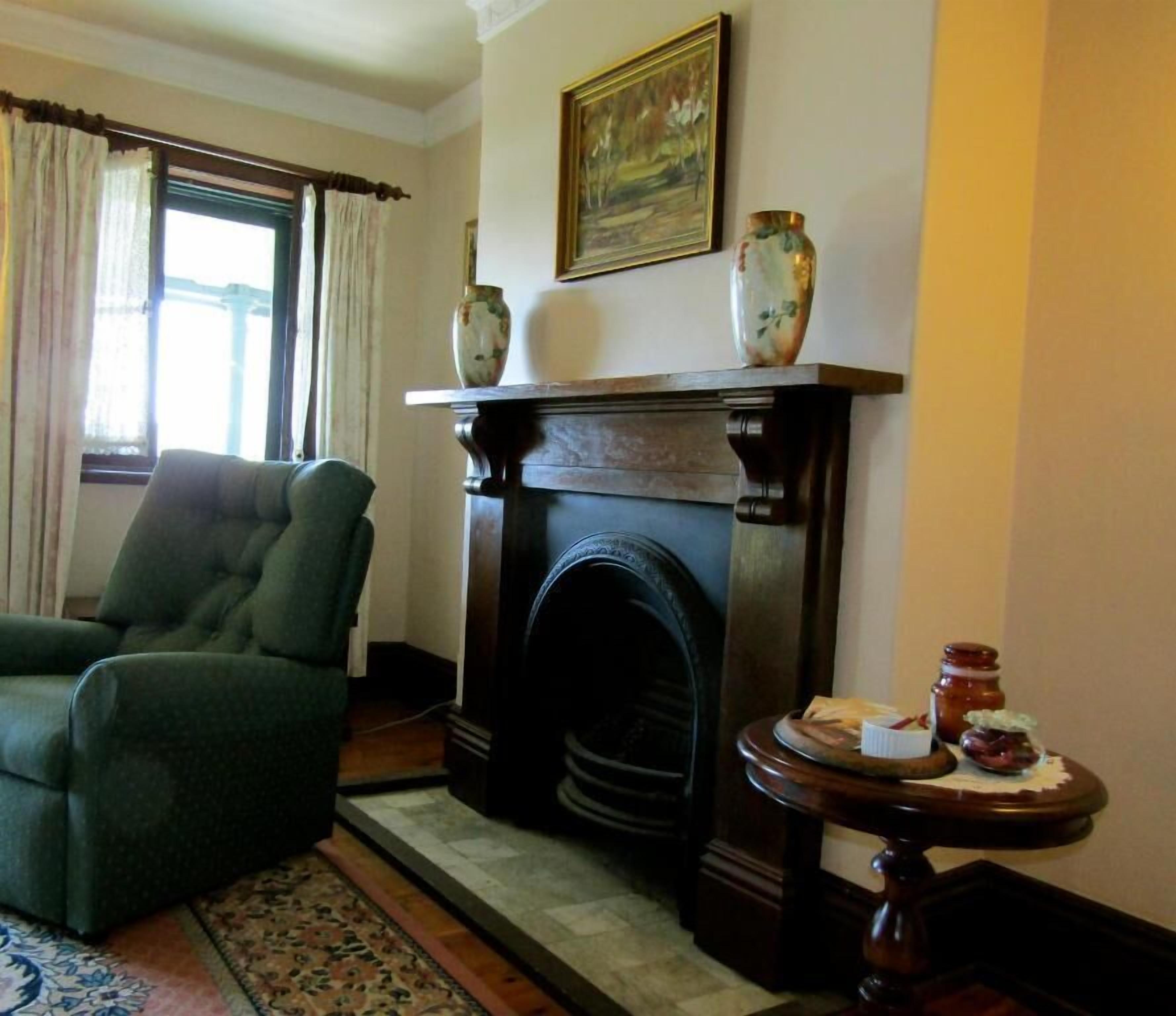 A living room with a green armchair, a fireplace, a painting, and a small table with jars.