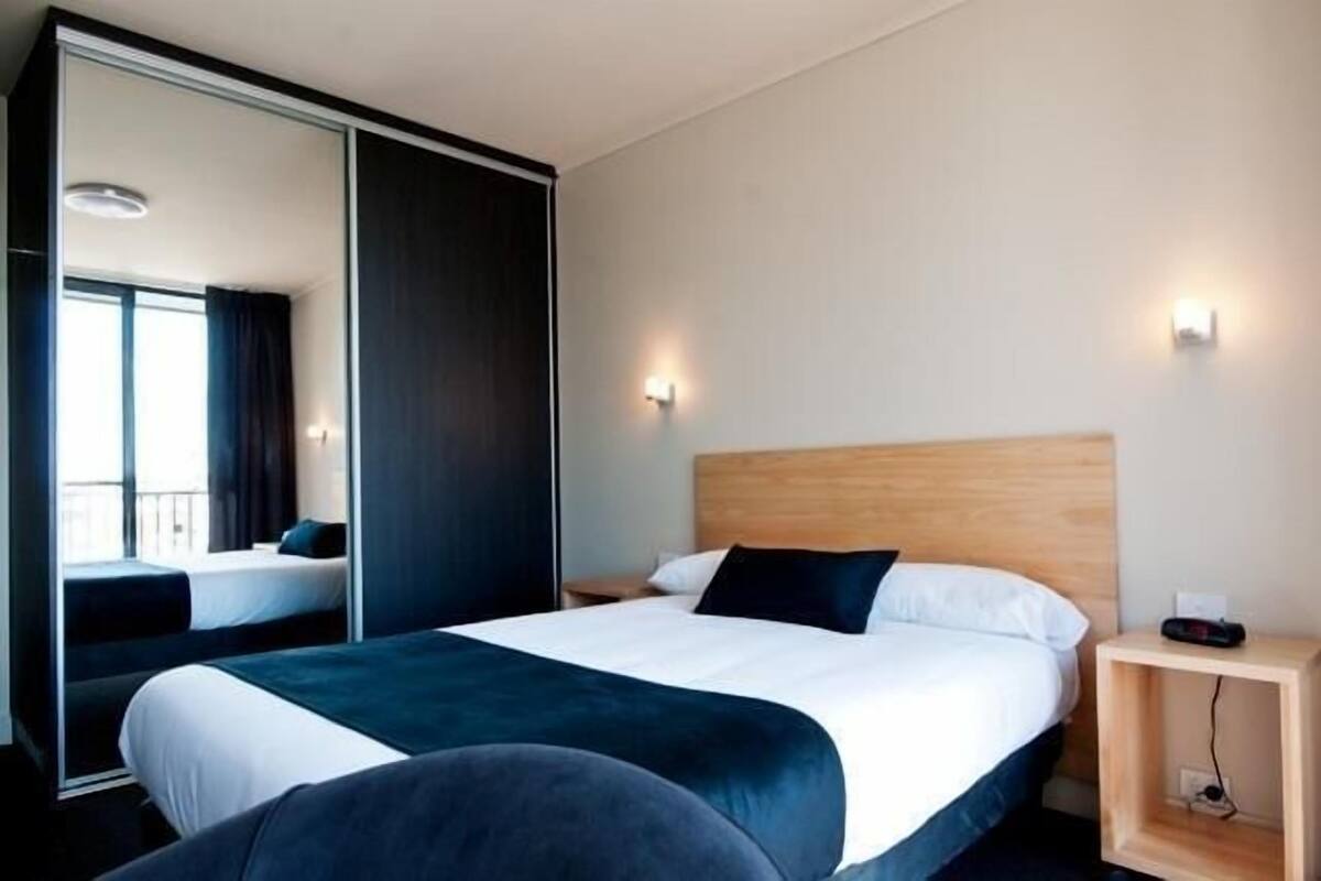 Hotellihuone, jossa on suuri sänky, yöpöytä, peili ja näkymä parvekkeelle.