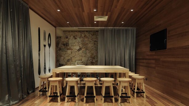 A conference room with a large wooden table surrounded by stools, a stone wall, wooden paneling, and a mounted television. - The Mansfield Park Hotel (Mansfield Park)