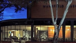 The Mansfield Park Hotel with a large glass facade, outdoor seating area, and a stone exterior. - The Mansfield Park Hotel (Mansfield Park)