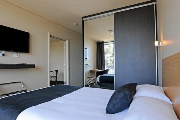 A modern hotel room with a large bed, a flat-screen TV mounted on the wall, and a sliding door leading to a balcony.