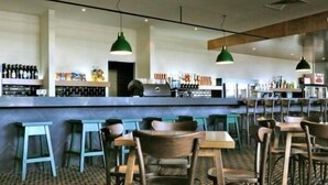 A modern bar area with high stools and tables, a counter with various bottles, and pendant lighting. - The Mansfield Park Hotel (Mansfield Park)