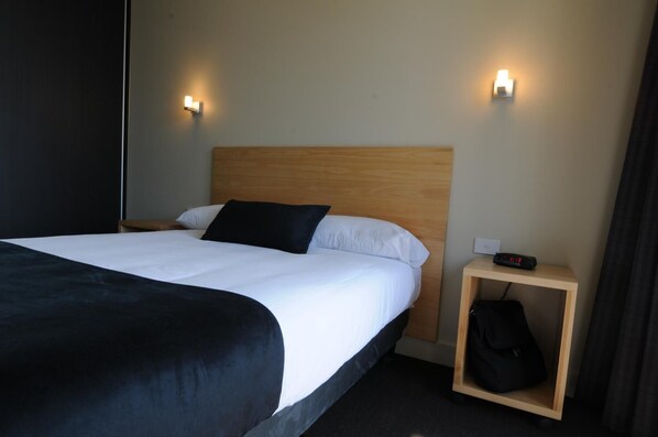 Une chambre d’hôtel avec un grand lit, deux tables de chevet, une petite table et un luminaire fixé au mur.