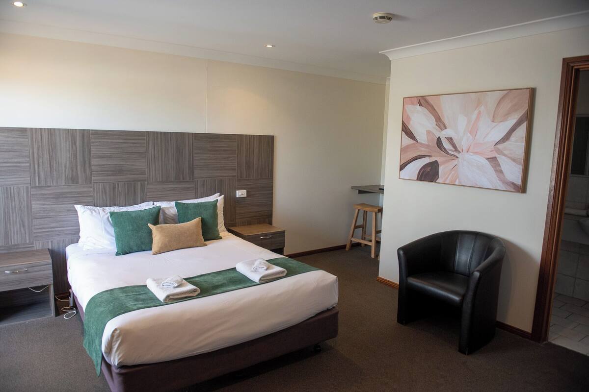 A hotel room with a large bed, a desk, a chair, and a painting on the wall.