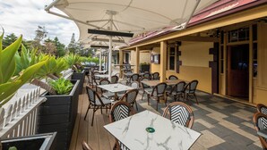 An outdoor cafe with tables and chairs, surrounded by planters and umbrellas. - Victoria Hotel - Strathalbyn (Strathalbyn)