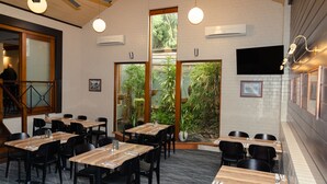 A restaurant with multiple tables and chairs, large windows with a view of greenery, and an air conditioning unit on the wall. - Victoria Hotel - Strathalbyn (Strathalbyn)