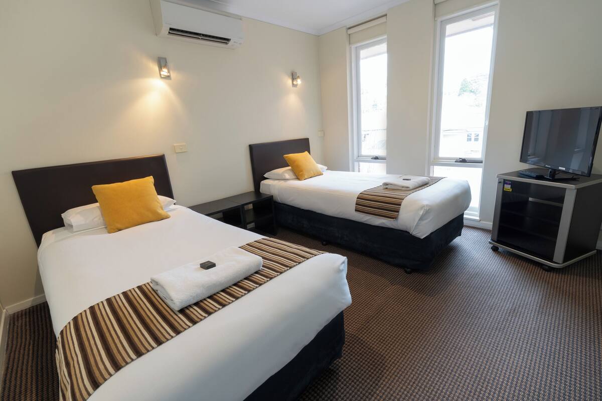 A hotel room with two beds, a TV, and a window.