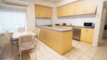 A kitchen with yellow cabinets, a central island, a dining table with chairs, and a microwave.