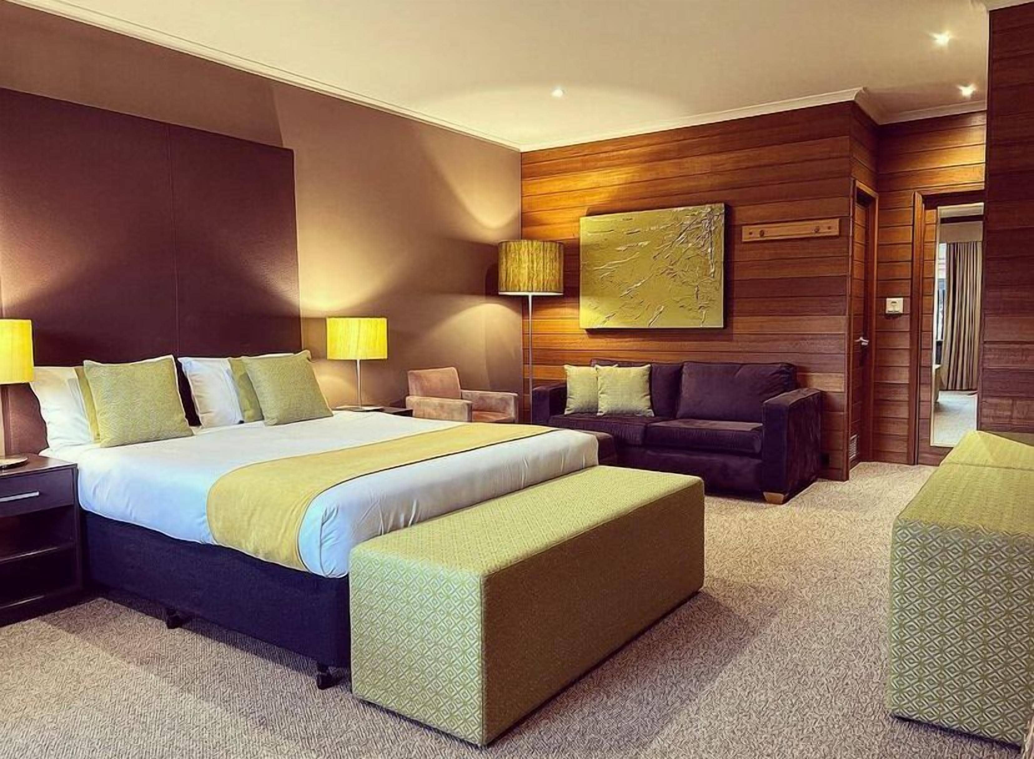 A modern hotel room with a large bed, a sofa, a chair, and a small table.