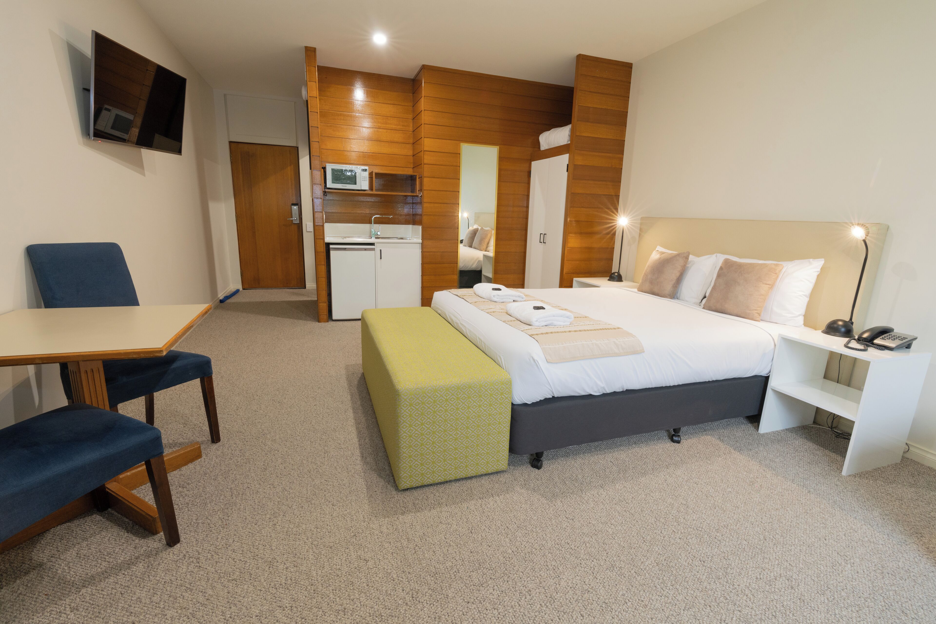 Una habitación de hotel con cama, mesita de noche, silla, escritorio y una pequeña cocina.