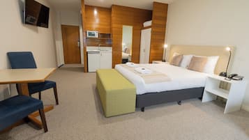 Una habitación de hotel con cama, mesita de noche, silla, escritorio y una pequeña cocina.