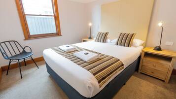 Ein ordentlich eingerichtetes Hotelzimmer mit einem großen Bett, zwei Nachttischen, einem Sessel und einem Fenster.