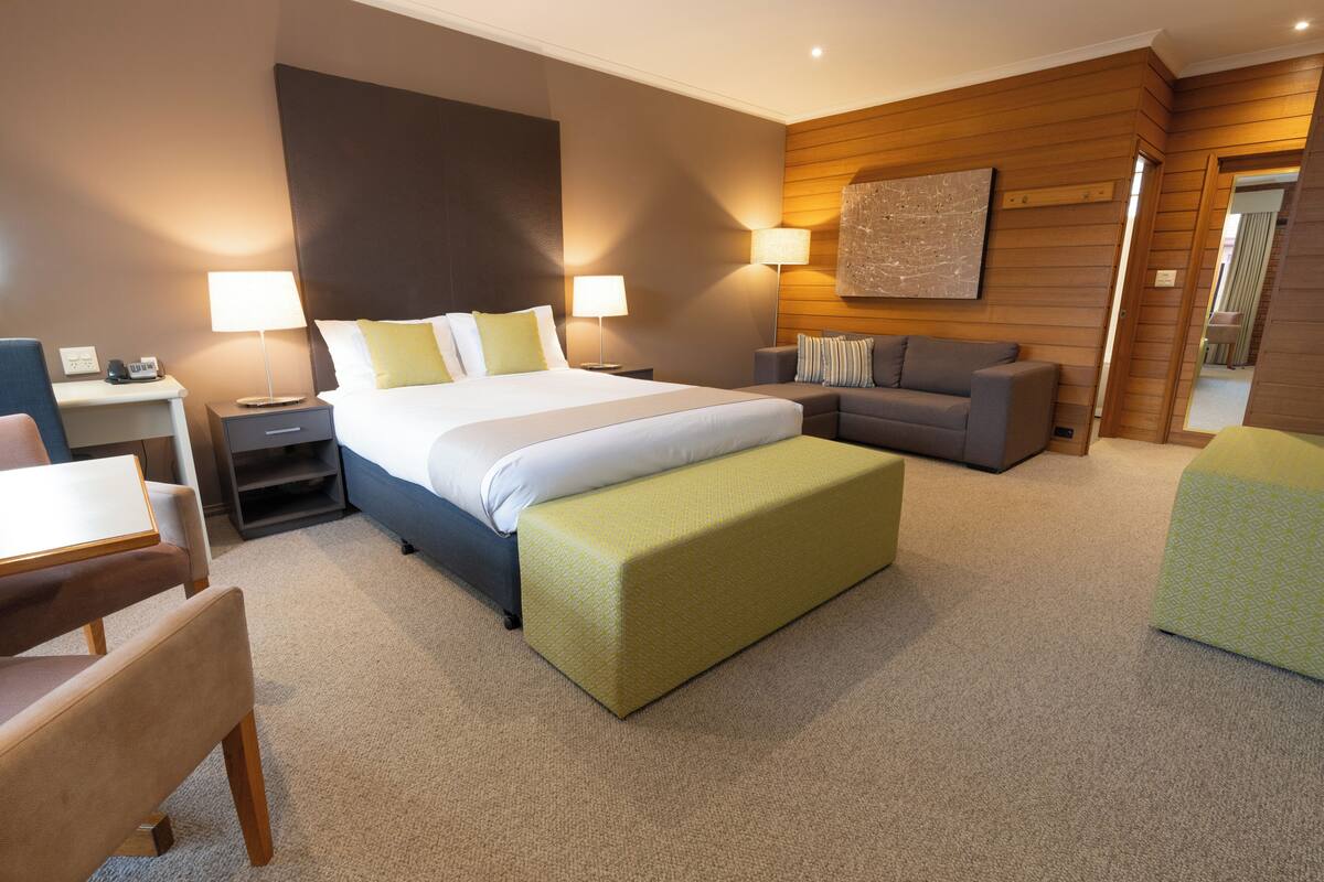 A modern hotel room with a large bed, a sofa, a desk, and a chair.