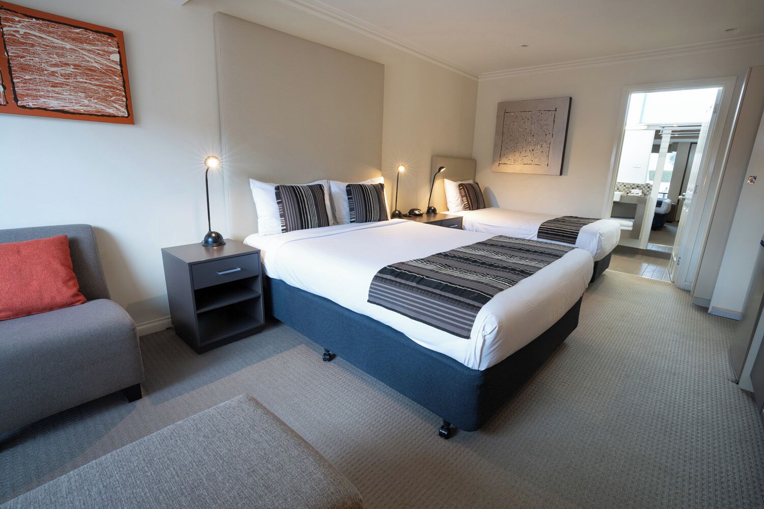 Quarto de hotel com cama de casal, mesas de cabeceira, uma cadeira, abajur e um quadro na parede.