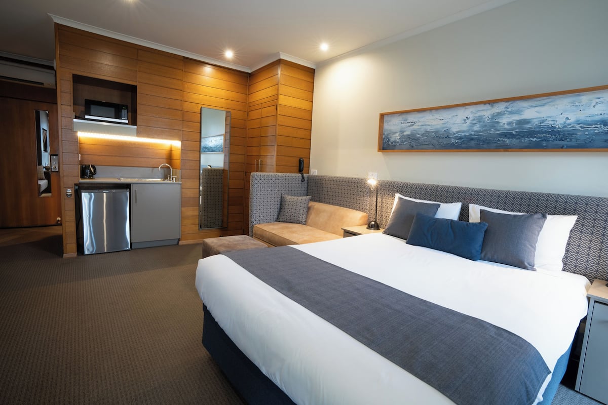 A hotel room with a large bed, a sofa, a desk, and a kitchenette.