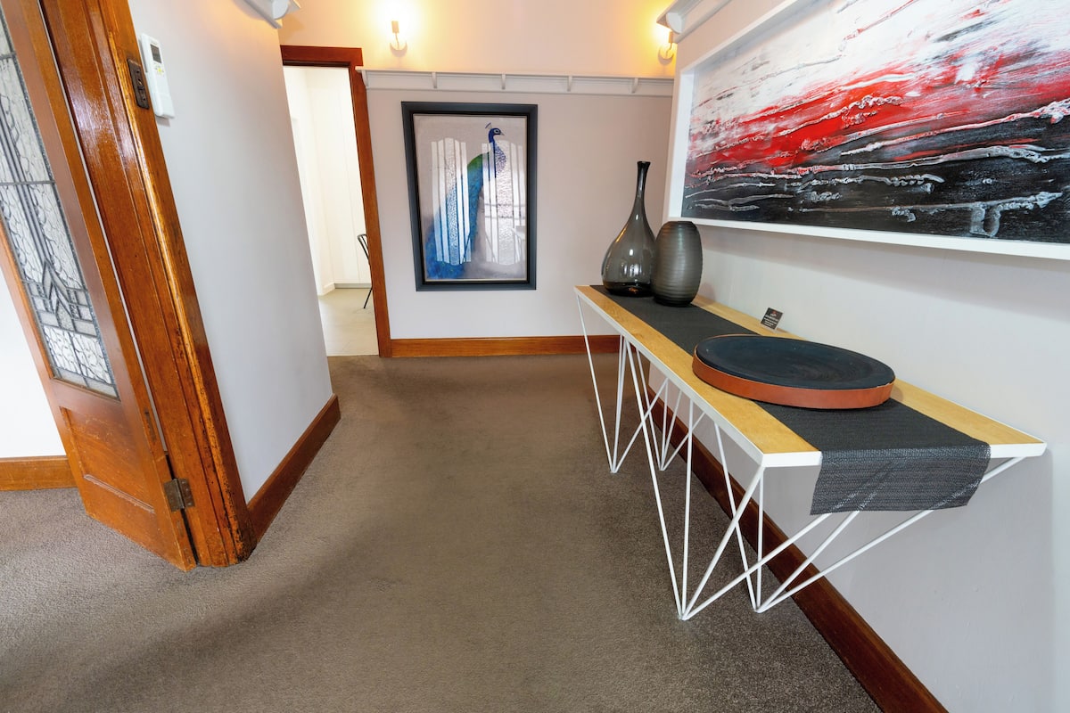 A hallway with a wooden door, a framed artwork, a modern console table with decorative items, and a large abstract painting on the wall.