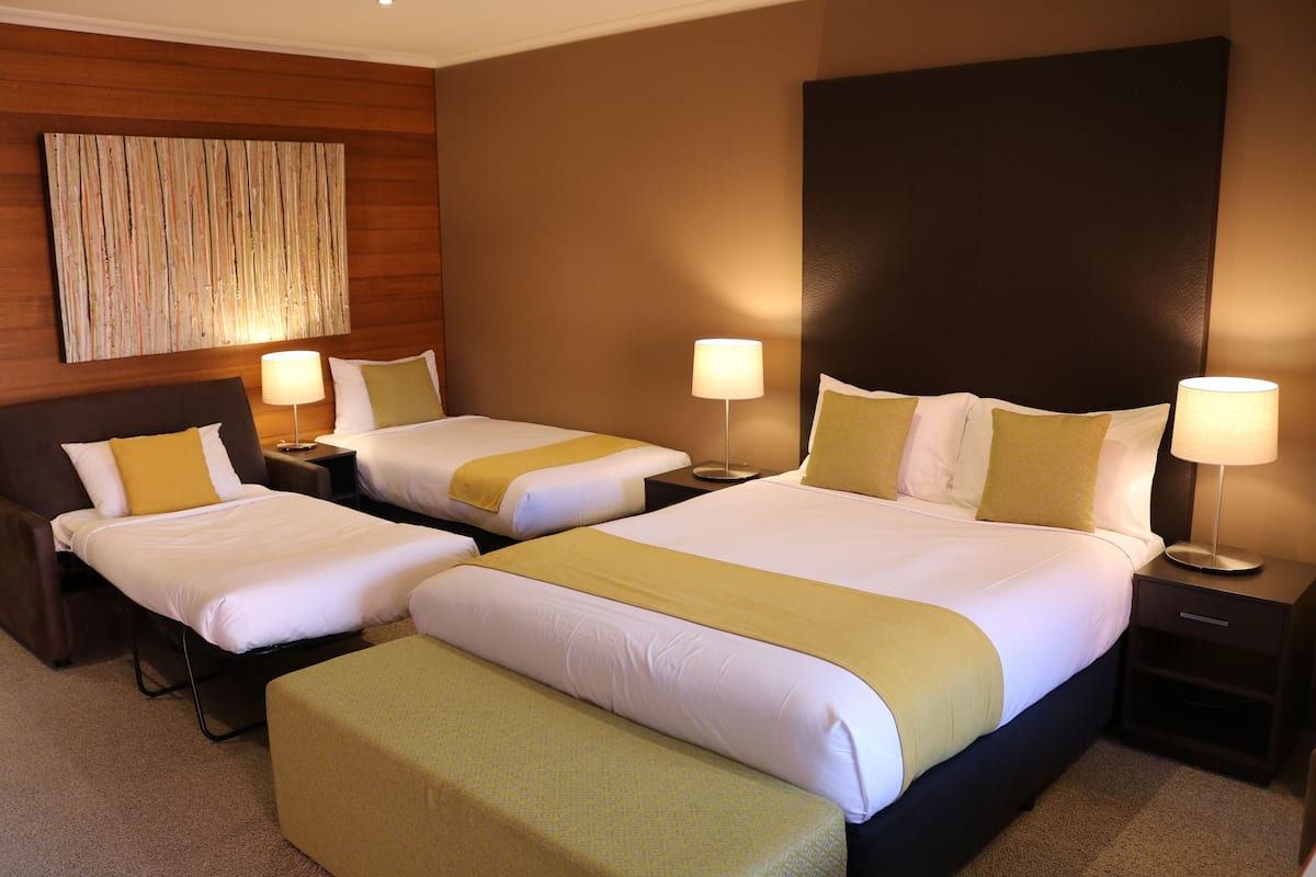 A hotel room with two beds, each with white linens and yellow accents, a large artwork on the wall, and a modern design.