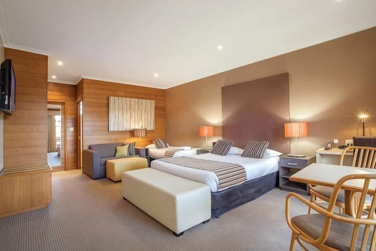 A hotel room with a large bed, a sofa, a dining table, and a TV.