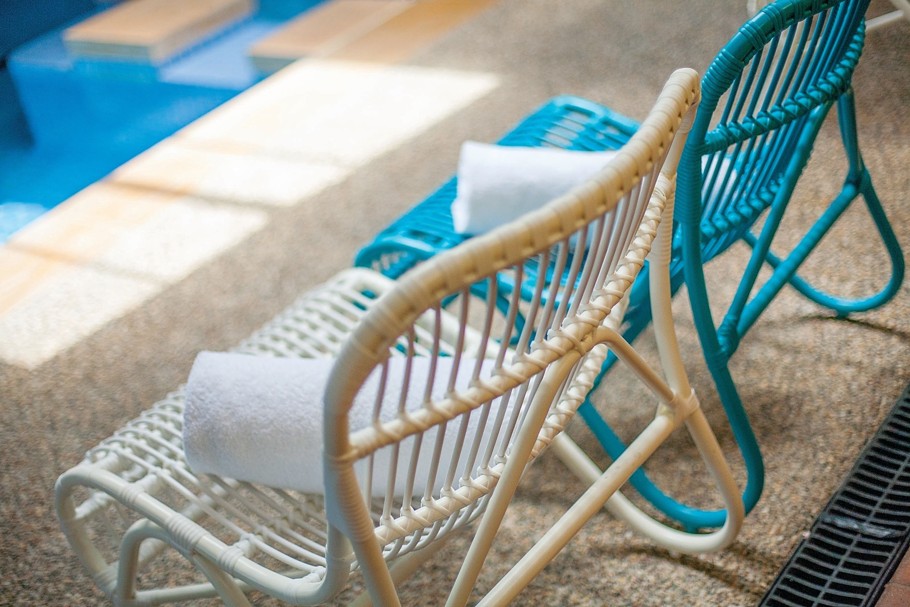 Zona de piscina con sillas reclinables de mimbre y una toalla blanca sobre una de ellas.