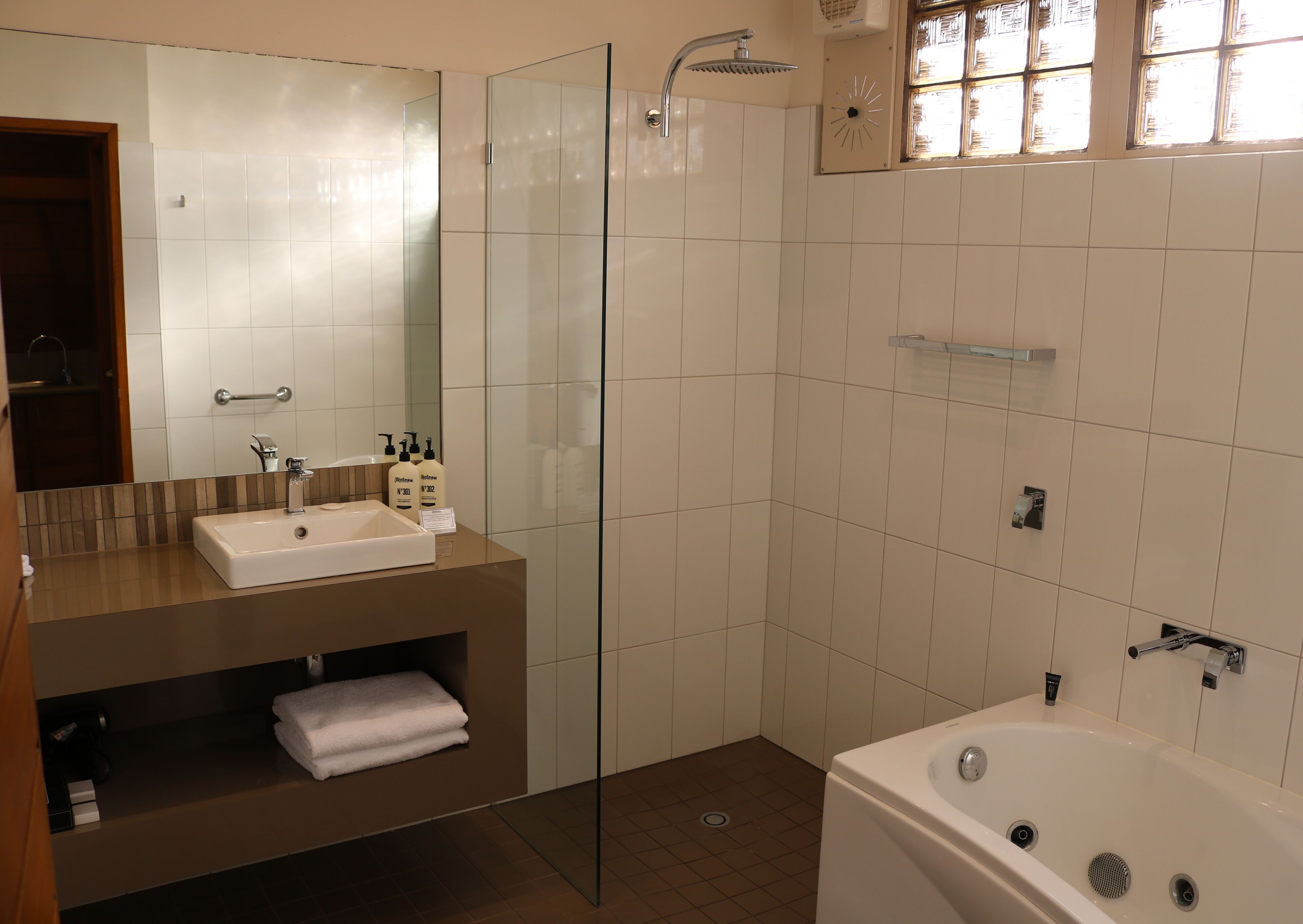 A modern bathroom with a glass shower enclosure, a white bathtub, and a vanity with a mirror and sink.