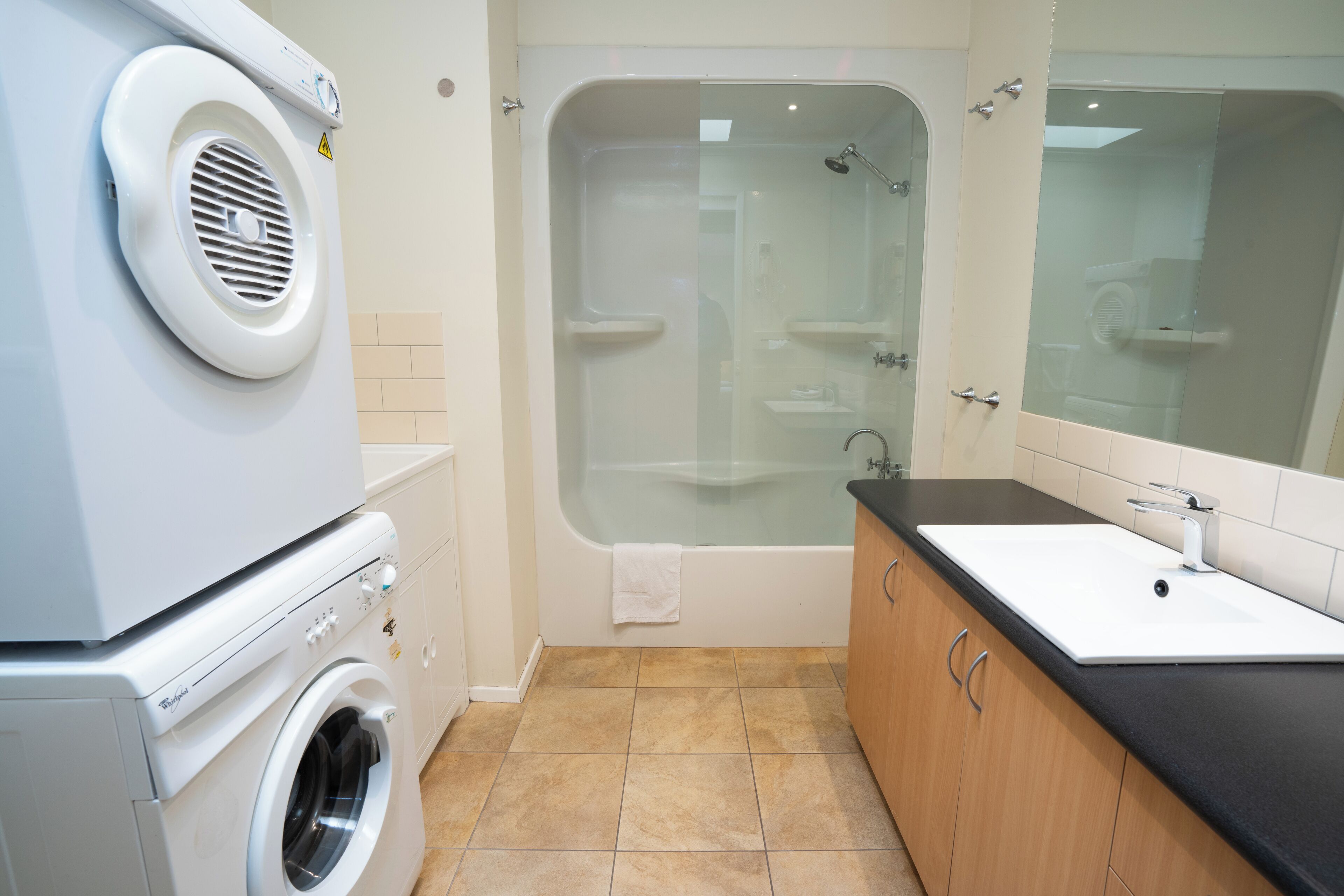 A compact bathroom with a washing machine, a glass-enclosed shower, and a sink with a black countertop.