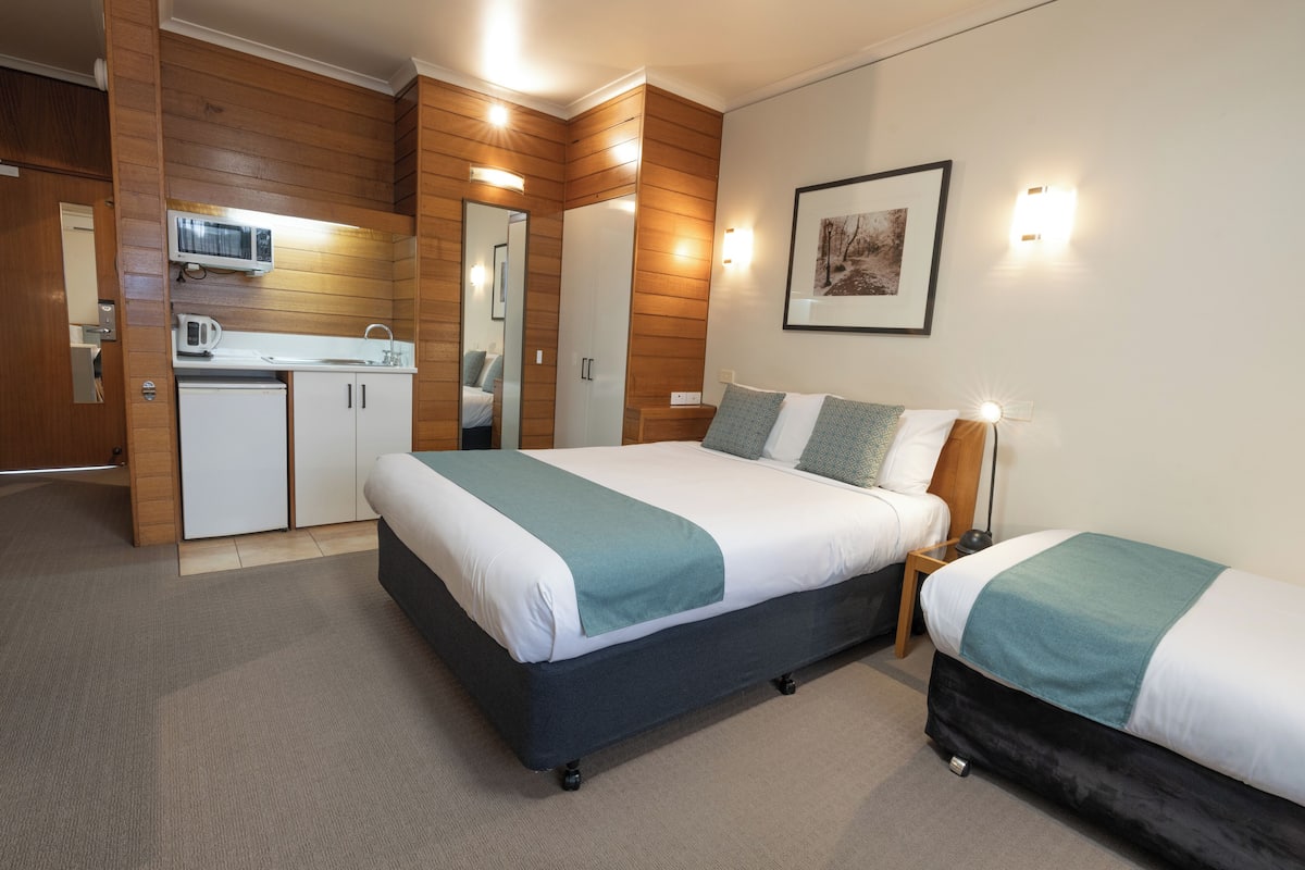 A hotel room with a large bed, a smaller bed, a kitchenette, and a bathroom.